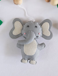 Adorable handcrafted felt elephant from the Baby Being baby cot mobile, surrounded by wooden accents and greenery for a calming nursery atmosphere.