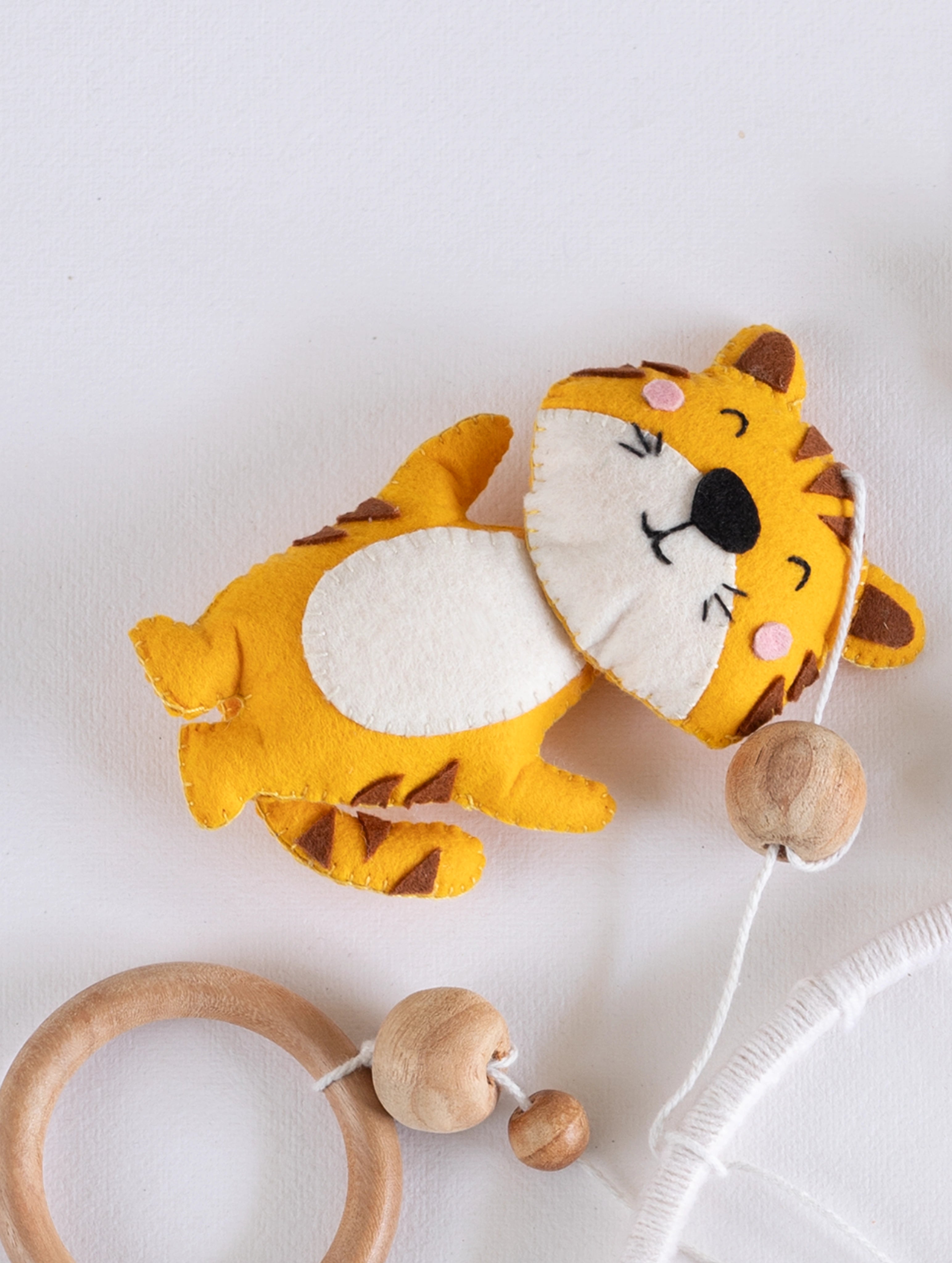 Soft handcrafted felt tiger ornament from the Baby Being crib mobile with natural wooden beads, designed for cheerful jungle-themed baby room décor.