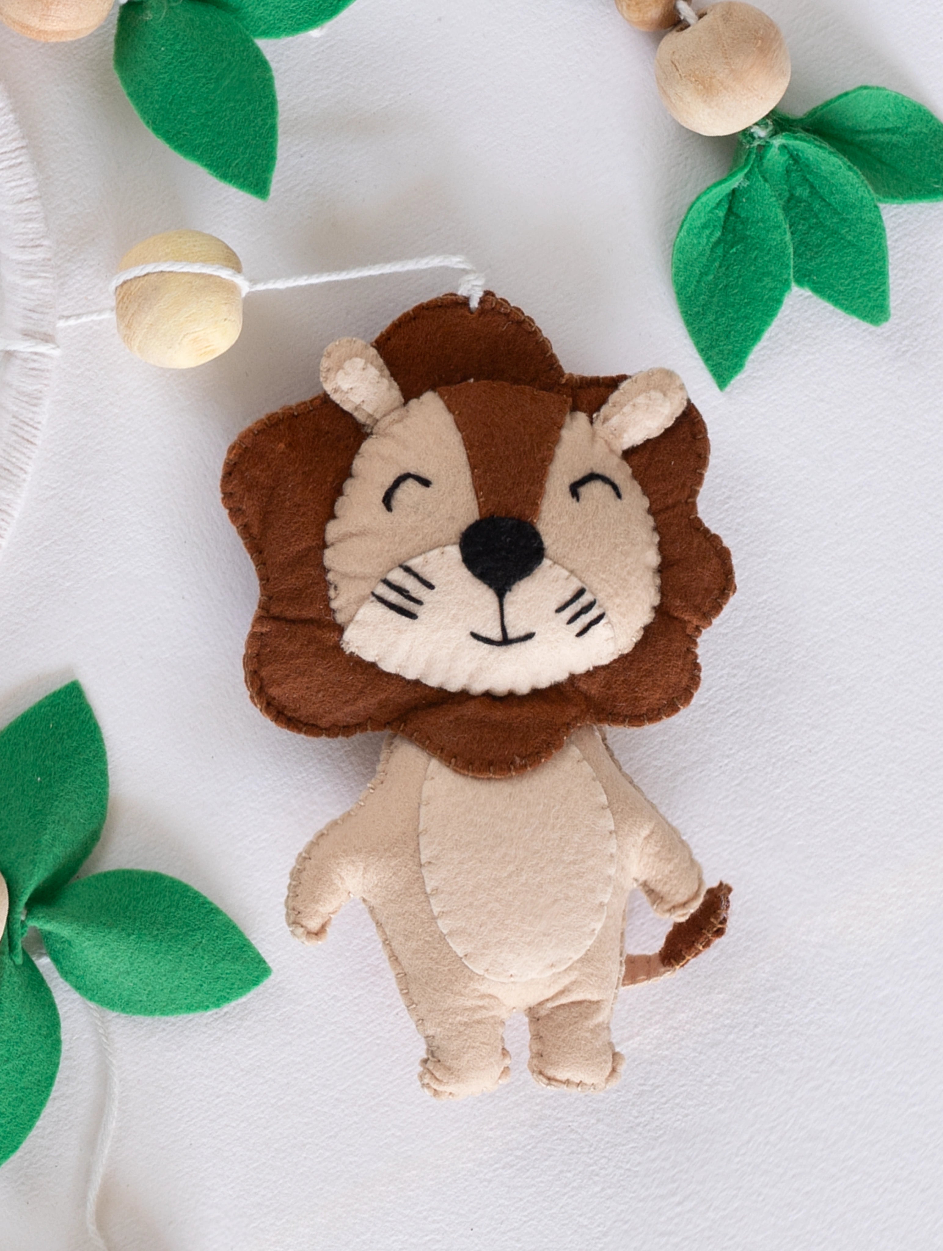 Smiling handcrafted felt lion ornament from the Baby Being nursery mobile, featuring soft textures and nature-inspired details for premium baby room décor.