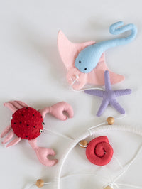 Flat lay of handcrafted felt crab, stingray, spiral shell, and starfish from the Deep in the Ocean baby mobile collection for ocean-inspired nursery décor.