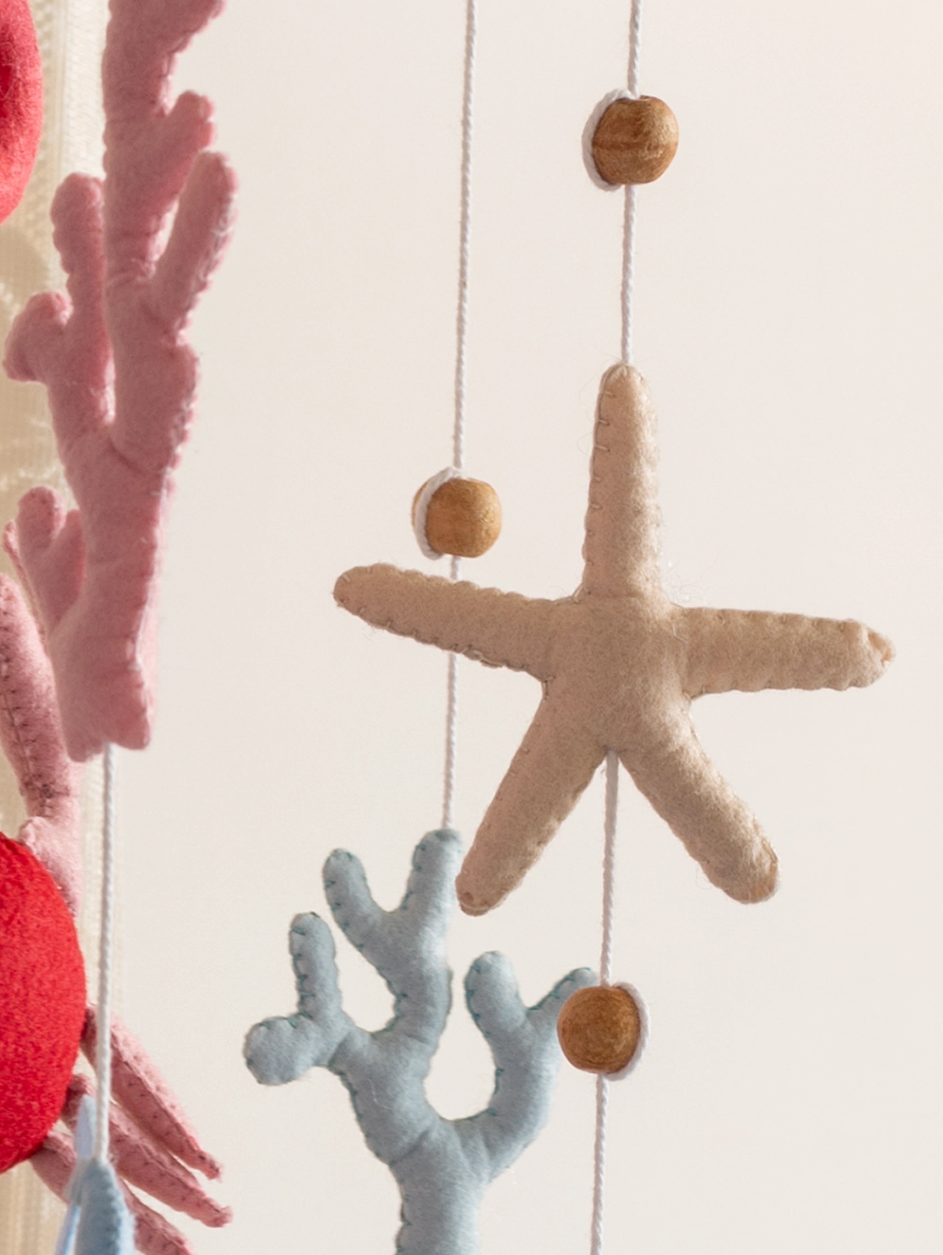 Handcrafted felt starfish with pastel coral details from the Deep in the Ocean baby crib mobile, designed to add a soft coastal touch to nursery décor.