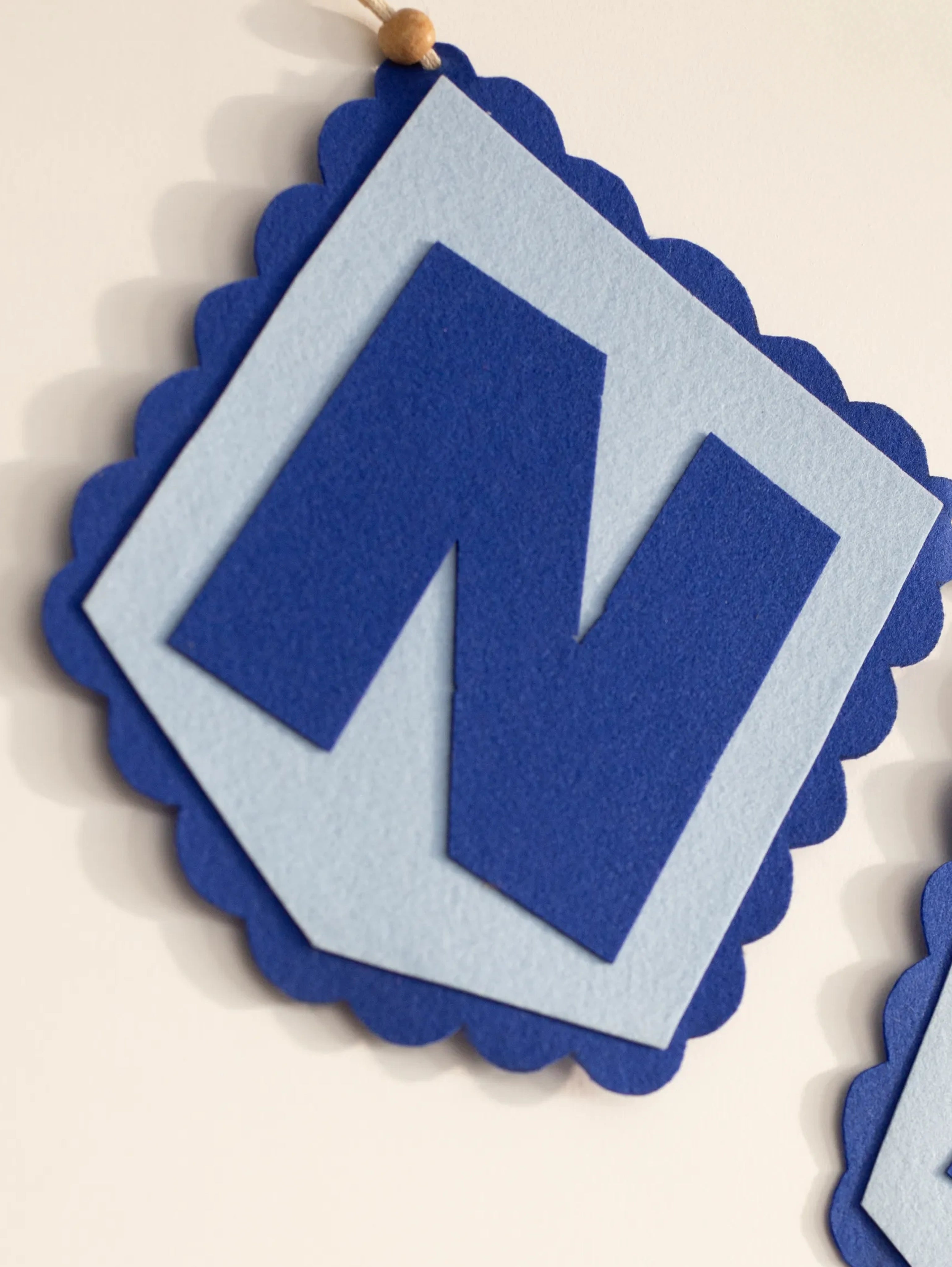 Macro close-up of the handcrafted blue felt letter "N" from a personalized baby name banner with scalloped edging.