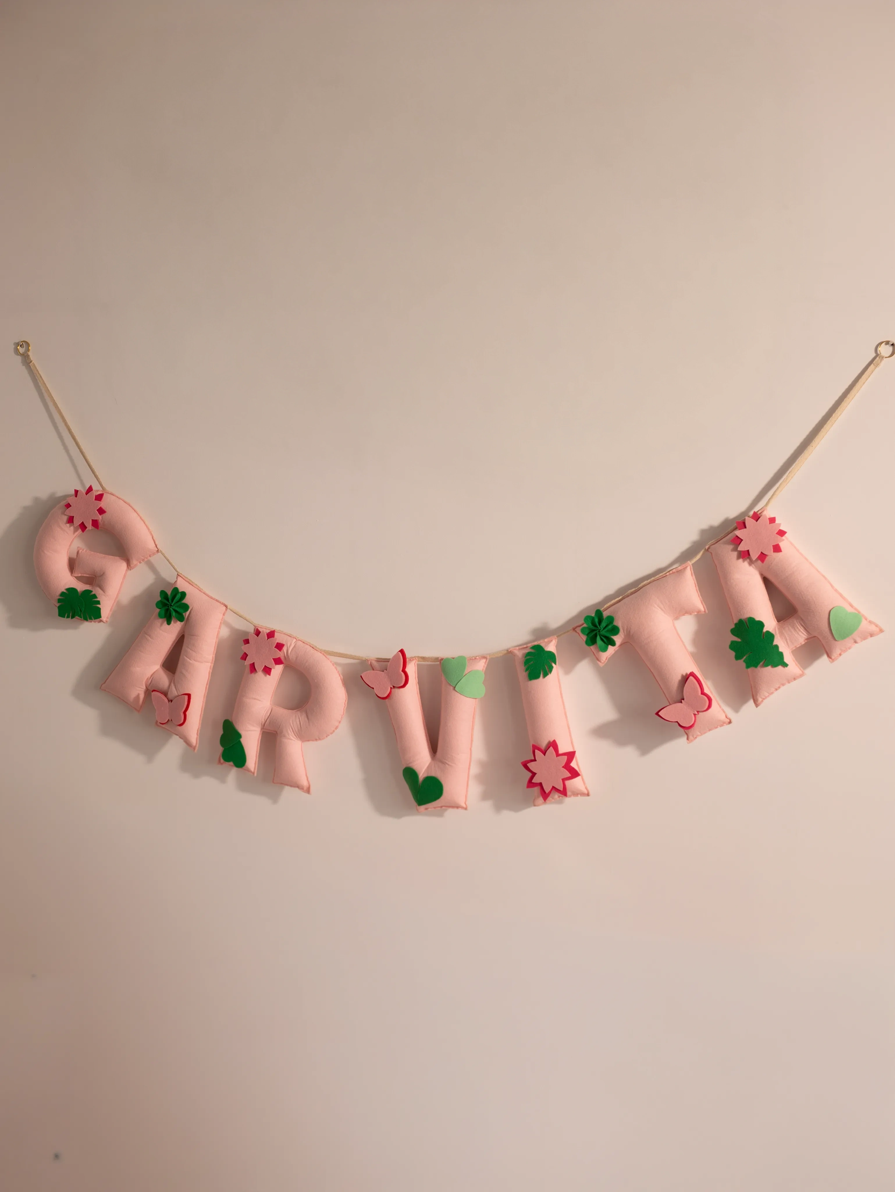 Garvita personalized blush pink felt name banner with handcrafted floral, butterfly and leaf accents for elegant baby nursery wall decor.