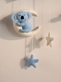 Close-up of a handcrafted blue koala felt ornament hanging from the personalized Taksh nursery name banner with star-themed decorations