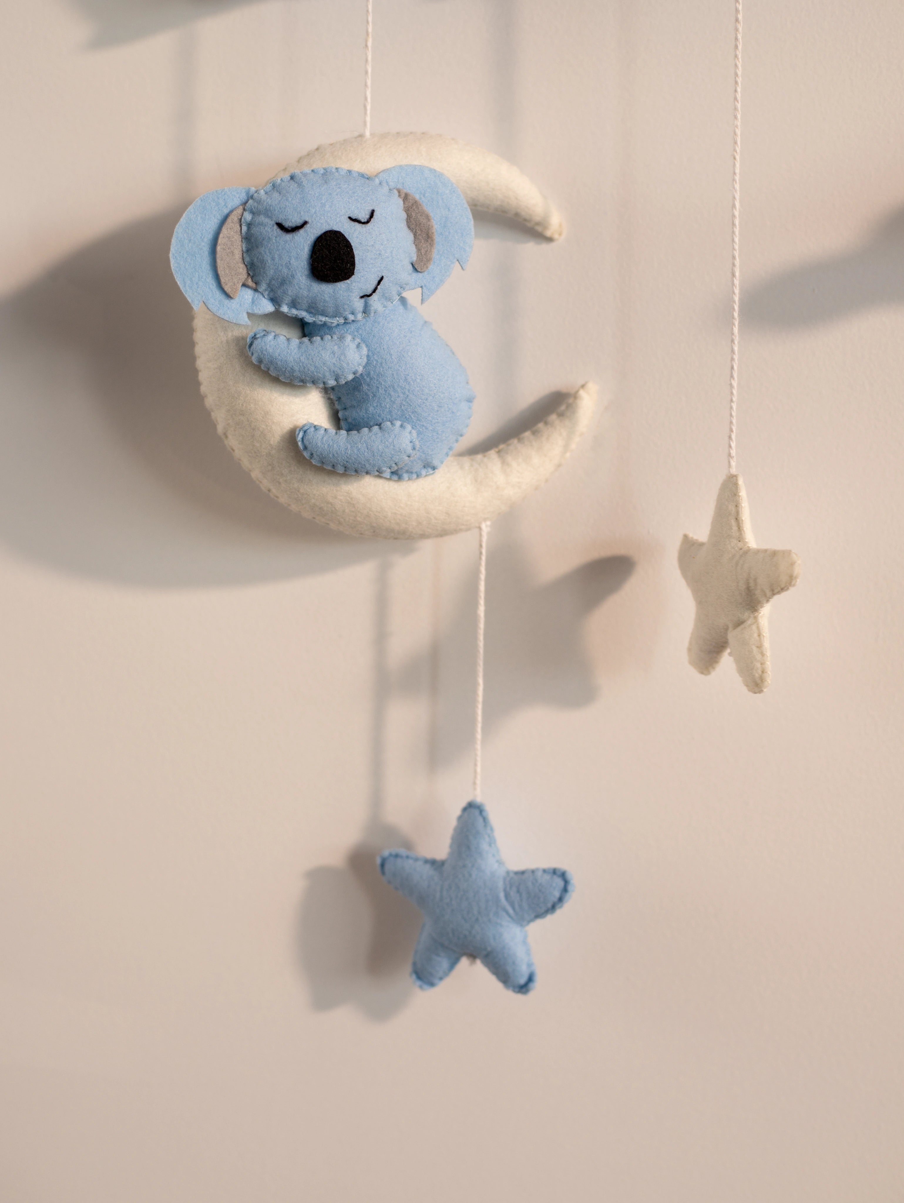 Close-up of a handcrafted blue koala felt ornament hanging from the personalized Taksh nursery name banner with star-themed decorations