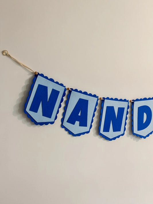 Close-up of the handcrafted Nandika blue felt name banner with scalloped flag-shaped letter pennants hanging on a natural cotton cord.
