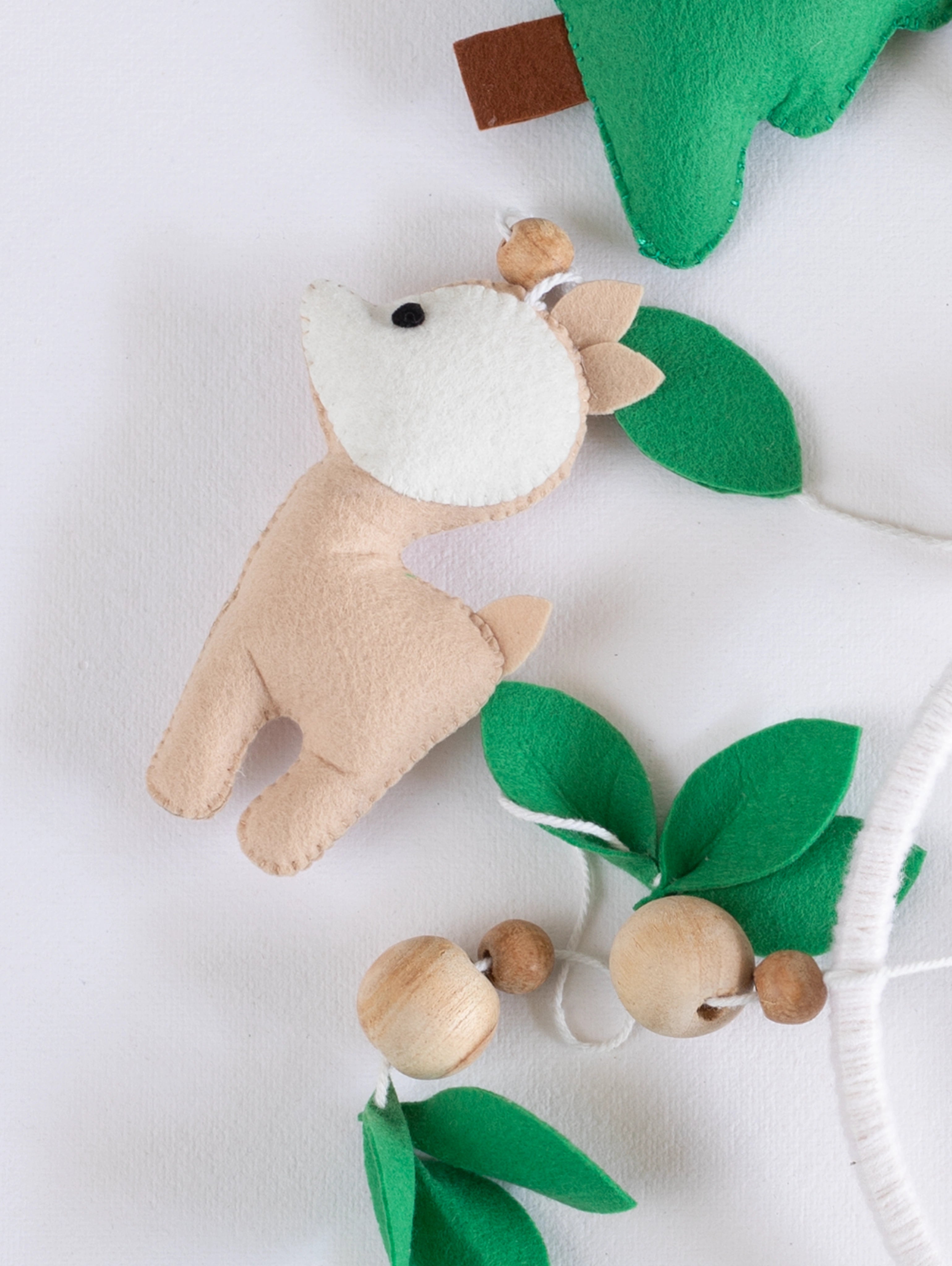 Soft handcrafted felt deer ornament with woodland leaf details from the Into the Wild baby cot mobile, creating a calm forest-themed nursery.