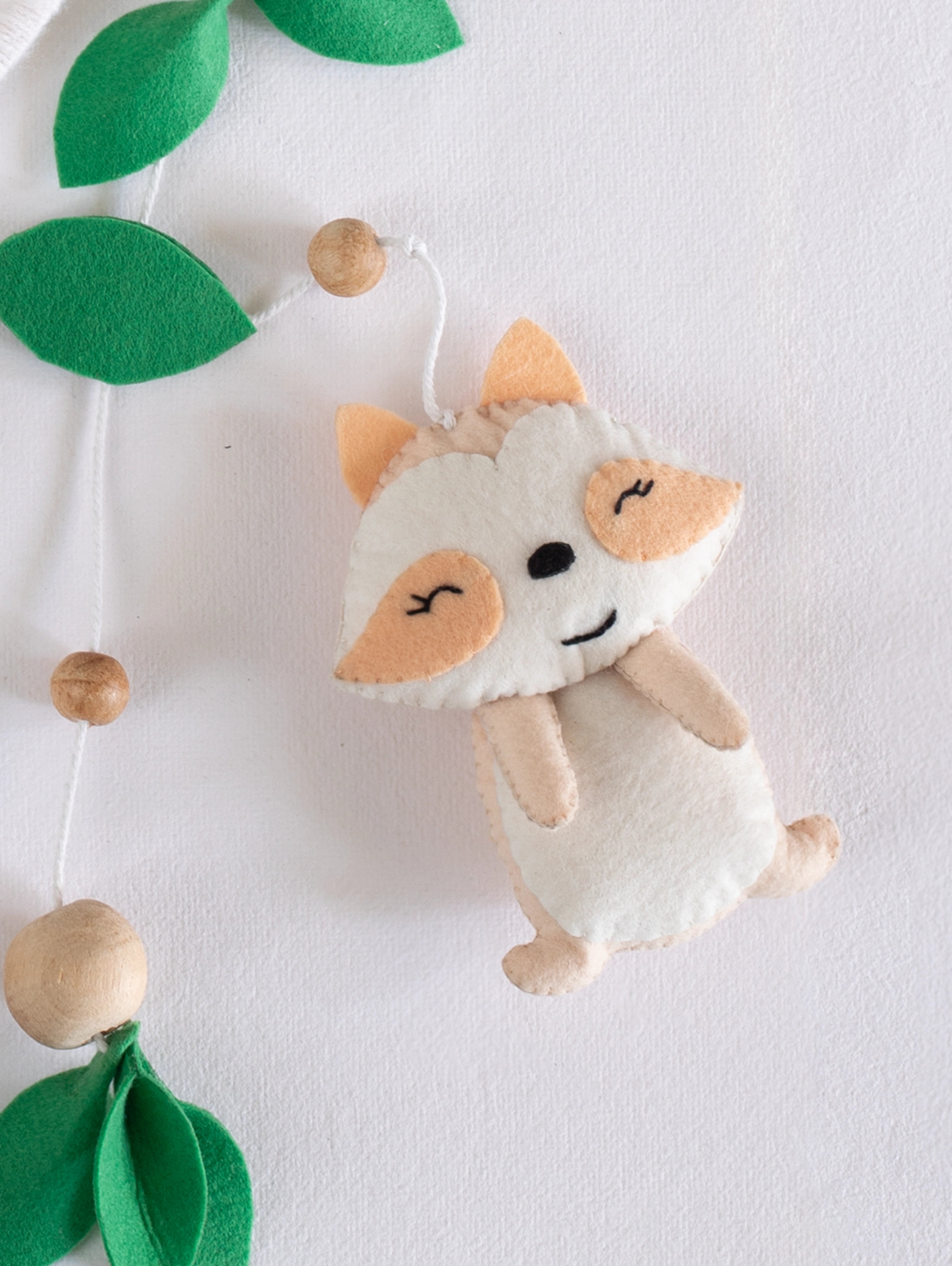 Cute handcrafted felt fox from the Into the Wild baby cot mobile, paired with leafy woodland accents for a warm and playful nursery atmosphere.