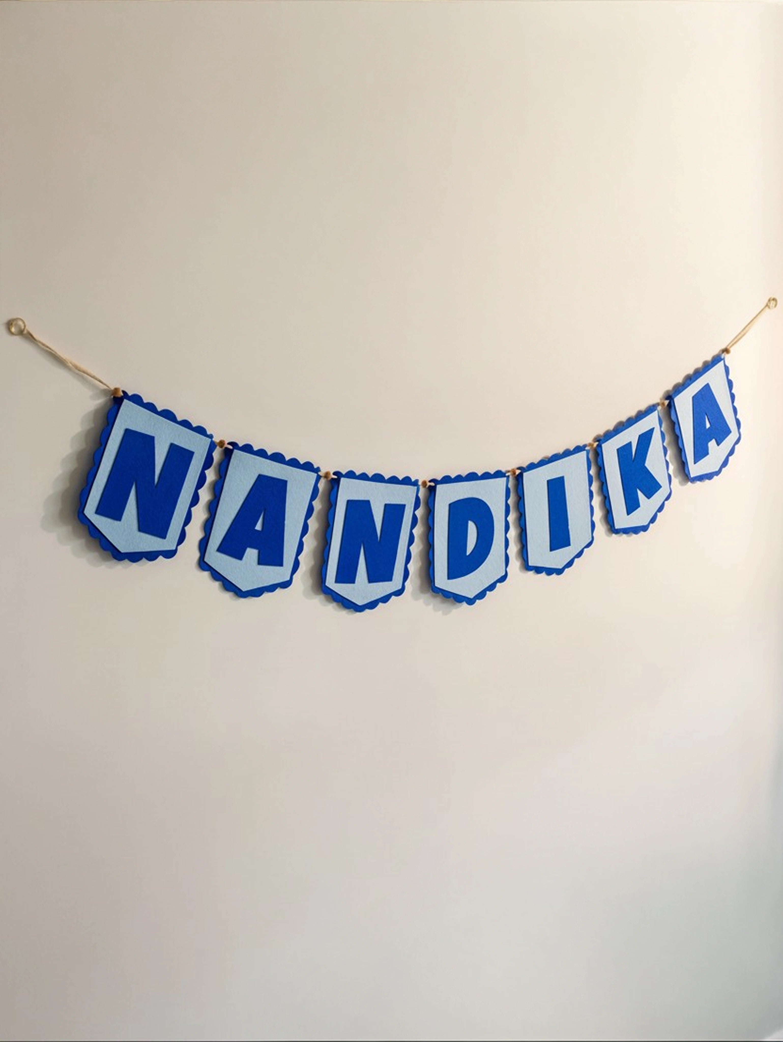 Personalized blue felt name banner spelling "Nandika" hanging on a nursery wall with handcrafted alphabet flags.
