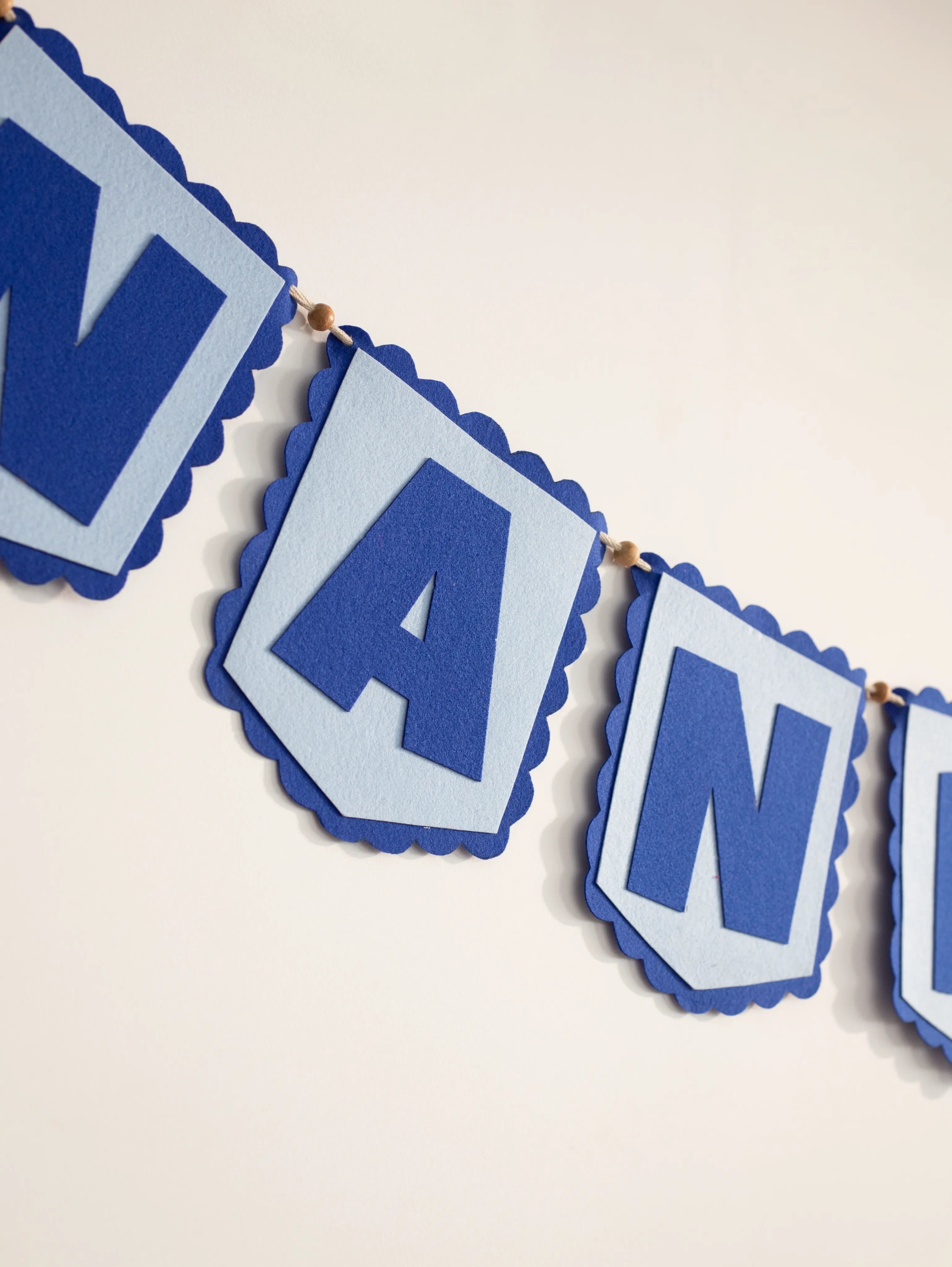 Close-up of the handcrafted blue felt "NAN" letters on a personalized baby name banner, showcasing premium nursery wall décor and detailed stitching.
