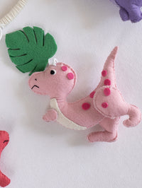 Soft handcrafted pink dinosaur ornament with felt jungle leaves from the Roar Away crib mobile, designed for whimsical dinosaur-themed baby nurseries.