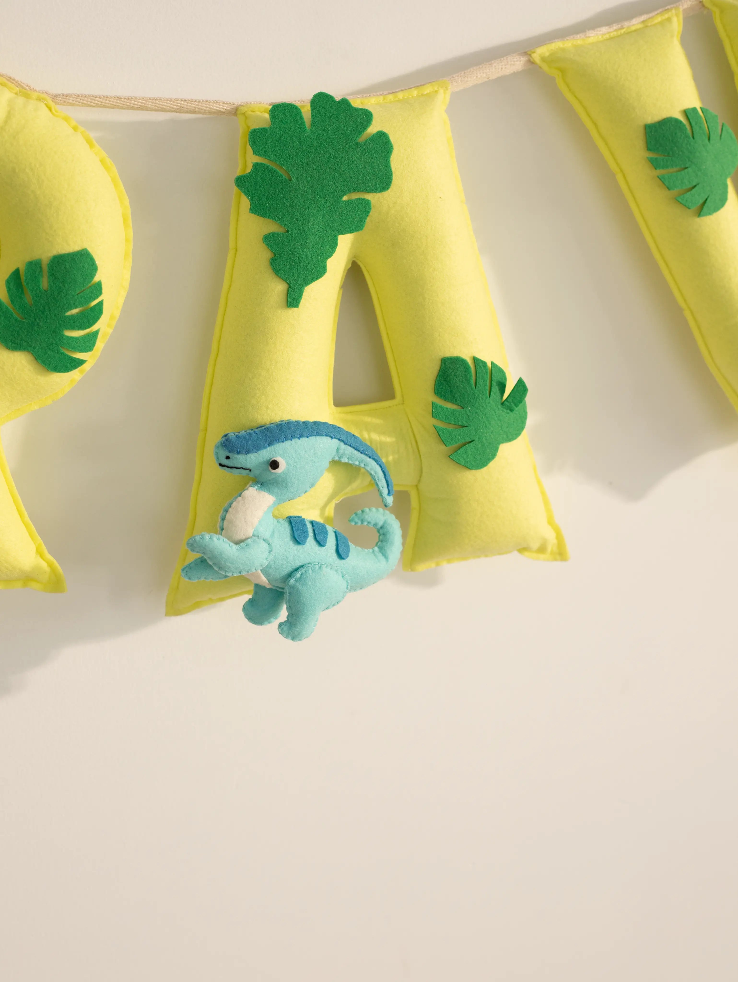 “Detailed view of the personalized Arav felt name banner showcasing yellow pennants with green leaf appliqués and a blue dinosaur accent.”