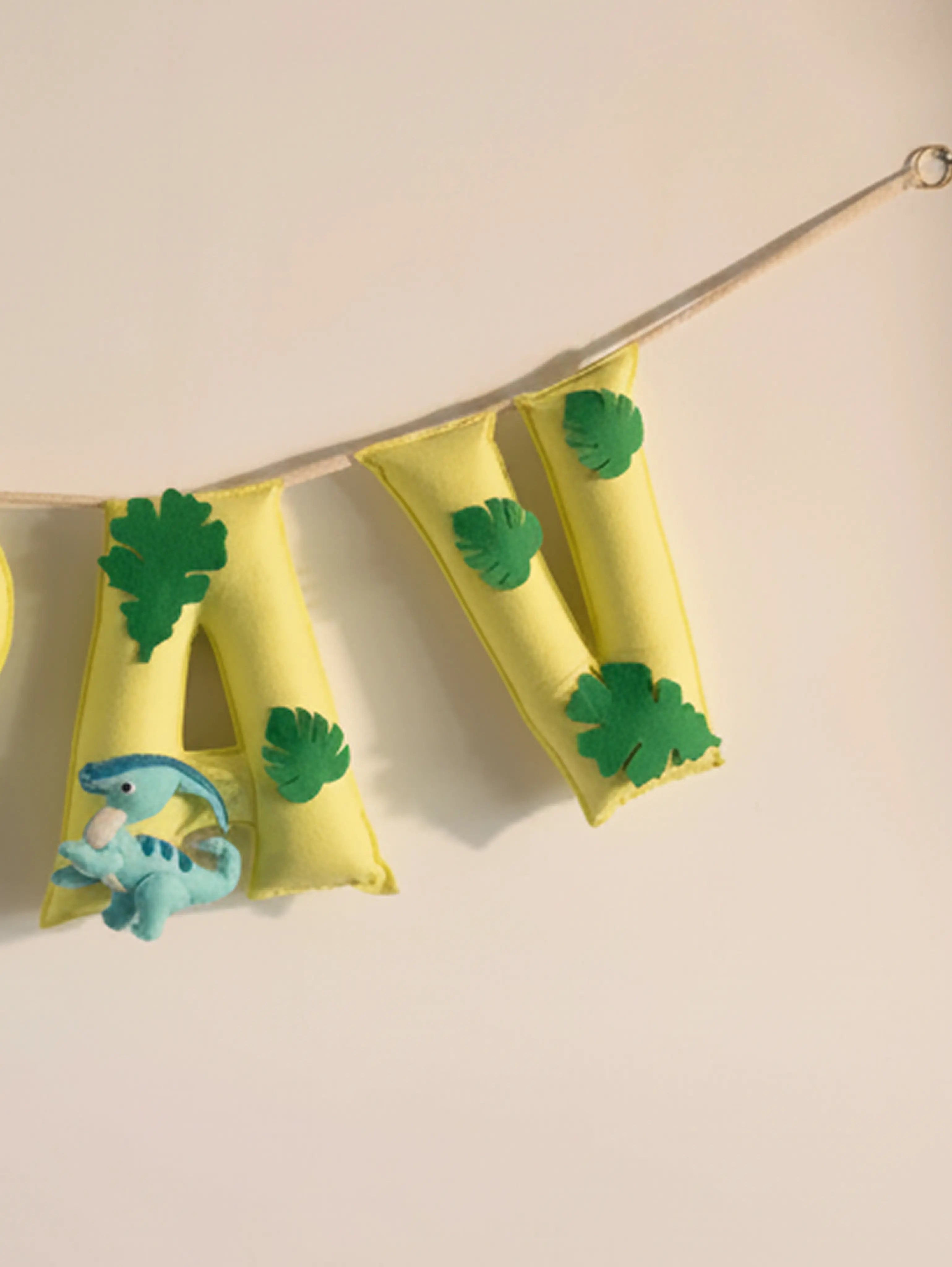 Close-up of the ending letters on the personalized Arav felt name banner featuring green leaf accents and yellow handcrafted flags.