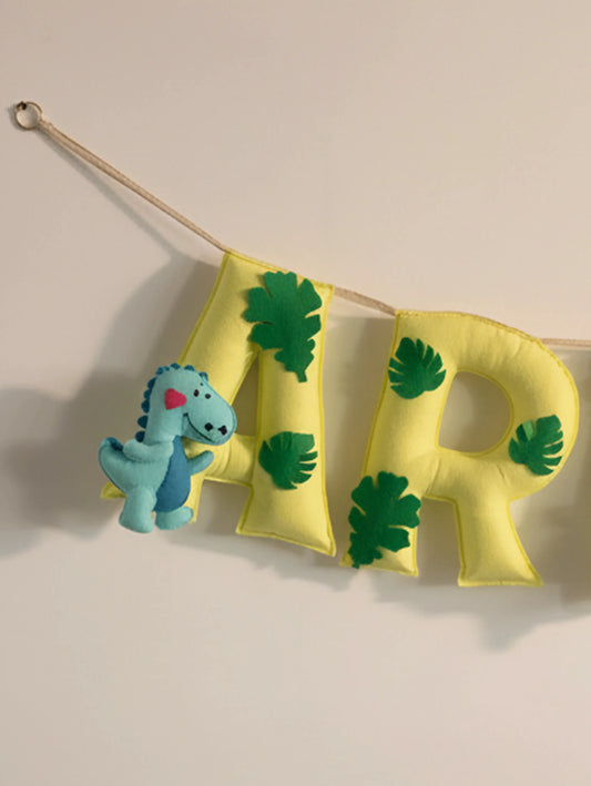 Close-up of the personalized Arav felt name banner showcasing green and yellow handcrafted letters with a blue dinosaur ornament