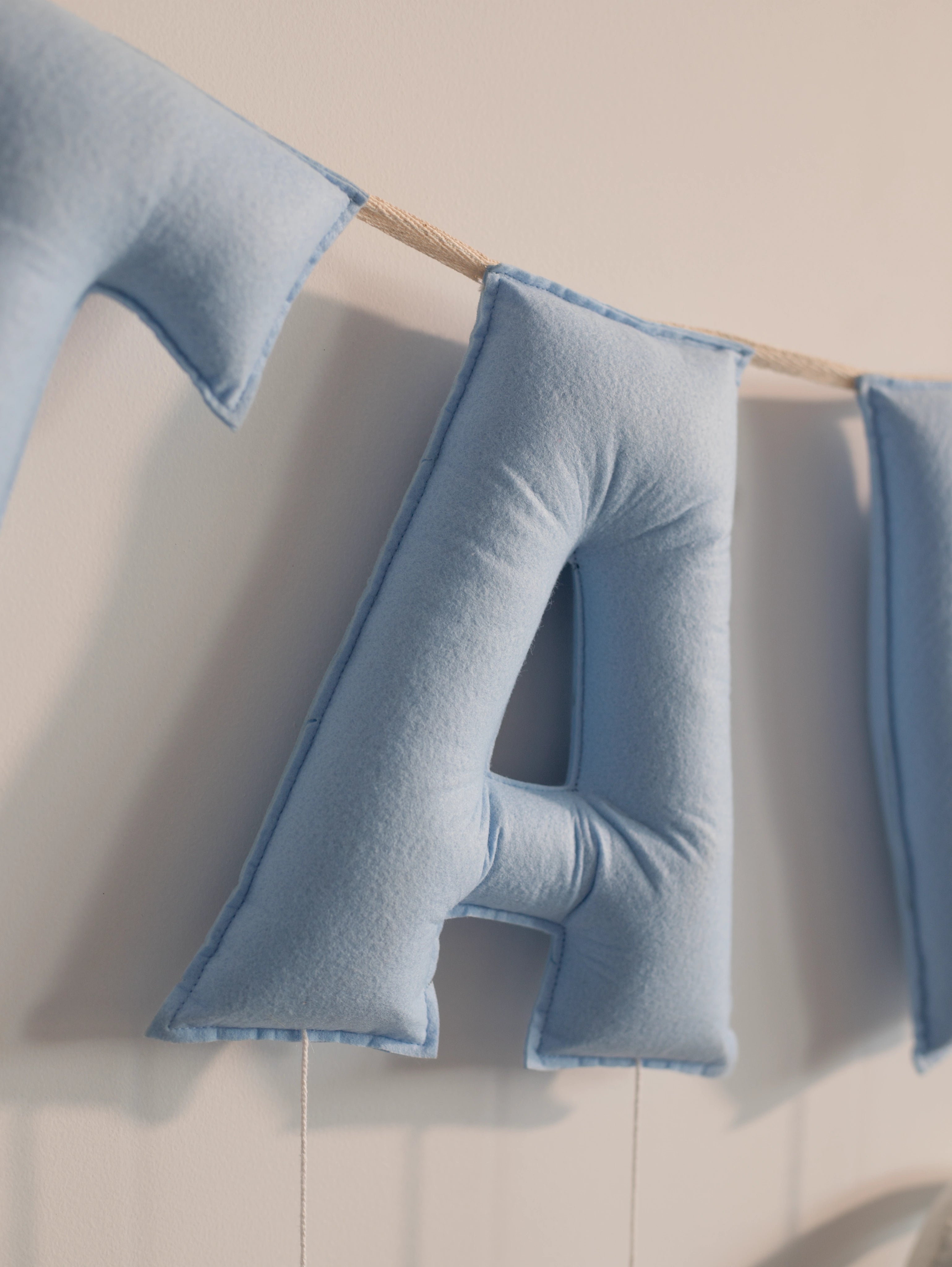 Close-up of the blue felt letter ‘A’ on the personalized Taksh nursery name banner with handcrafted stitching details