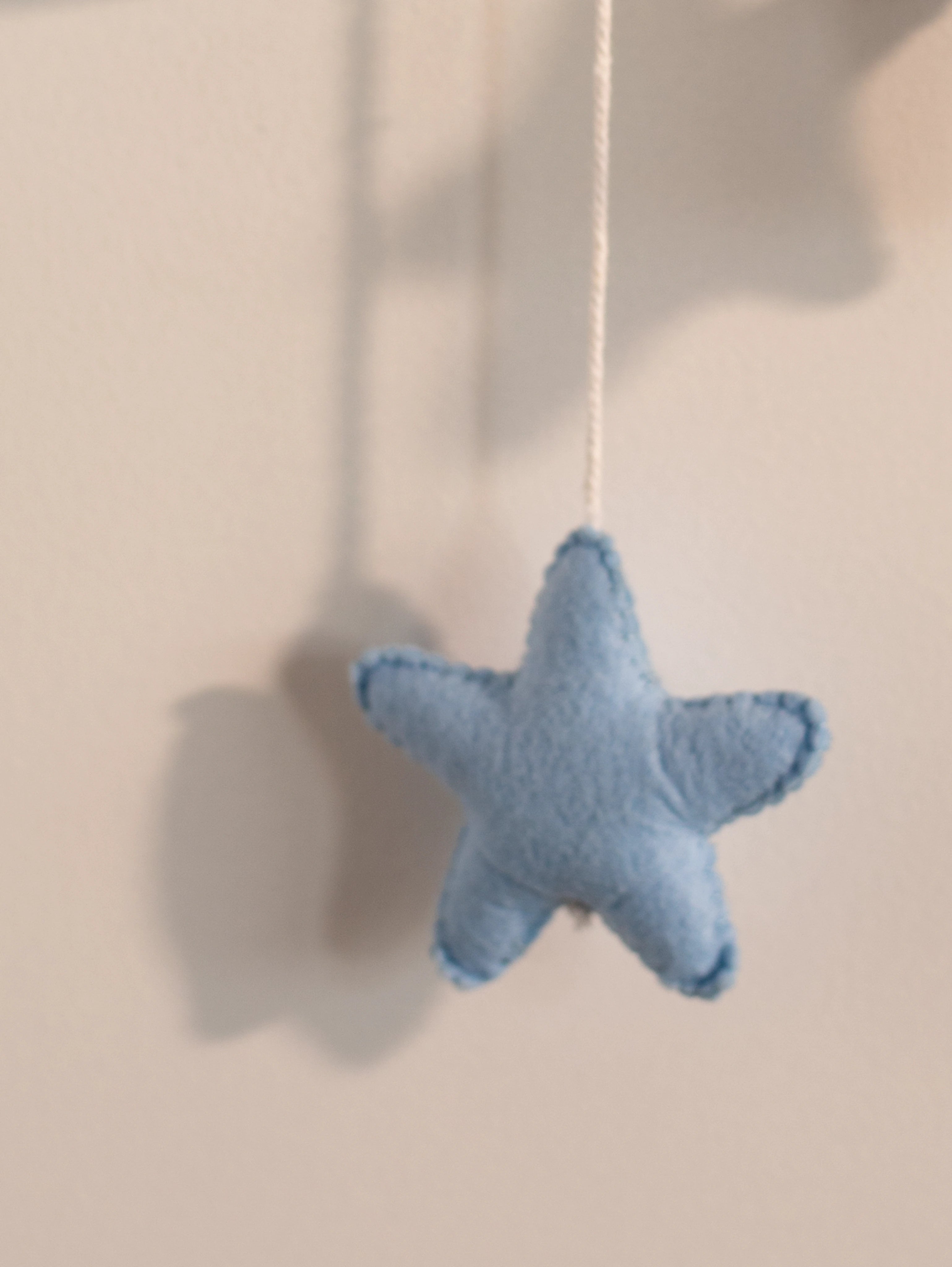 Close-up of a handcrafted blue felt star hanging ornament from a personalized baby nursery name banner.