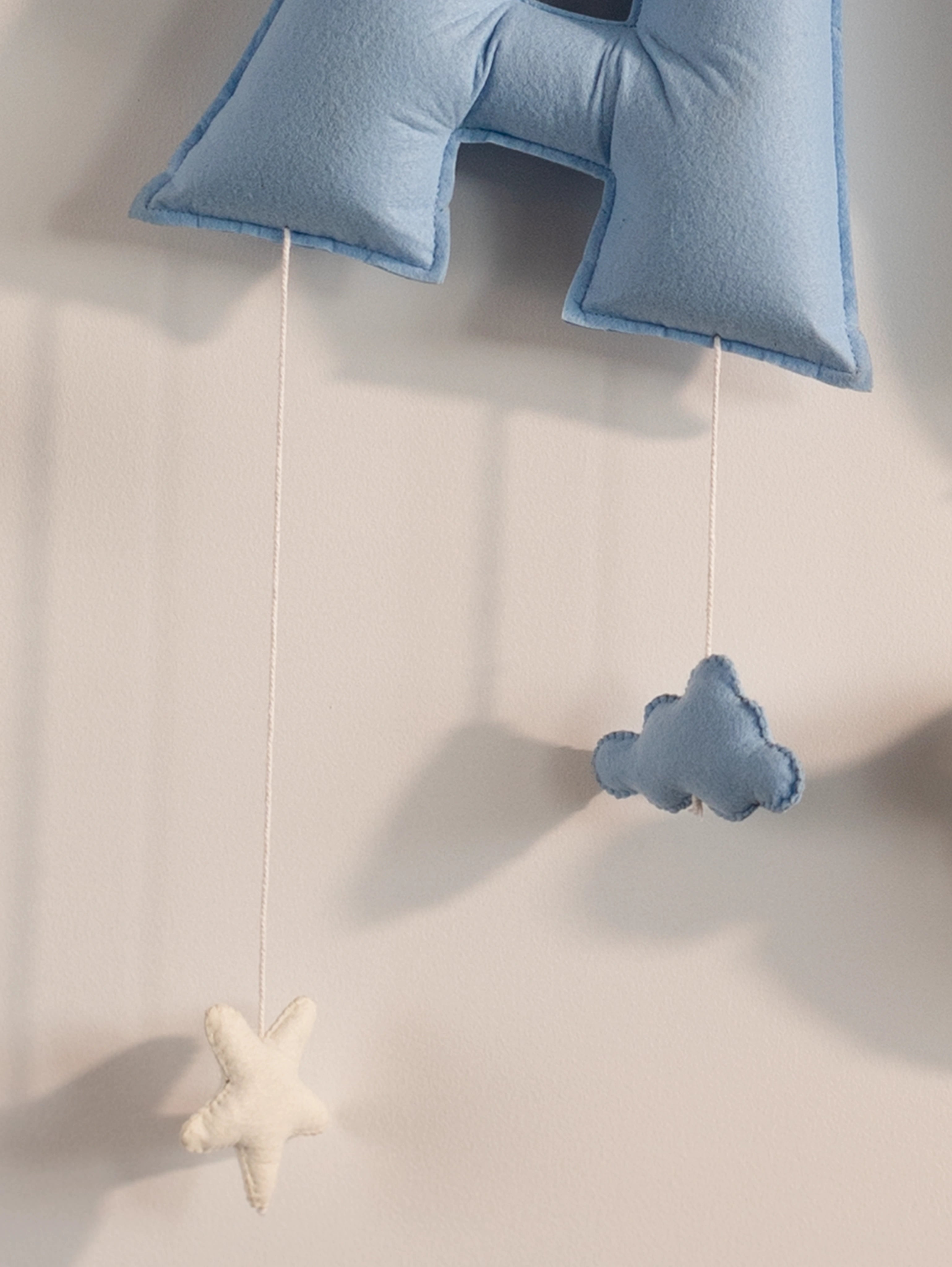 Detailed view of the lower blue felt letter with a handcrafted cloud ornament on the personalized Taksh baby name banner.