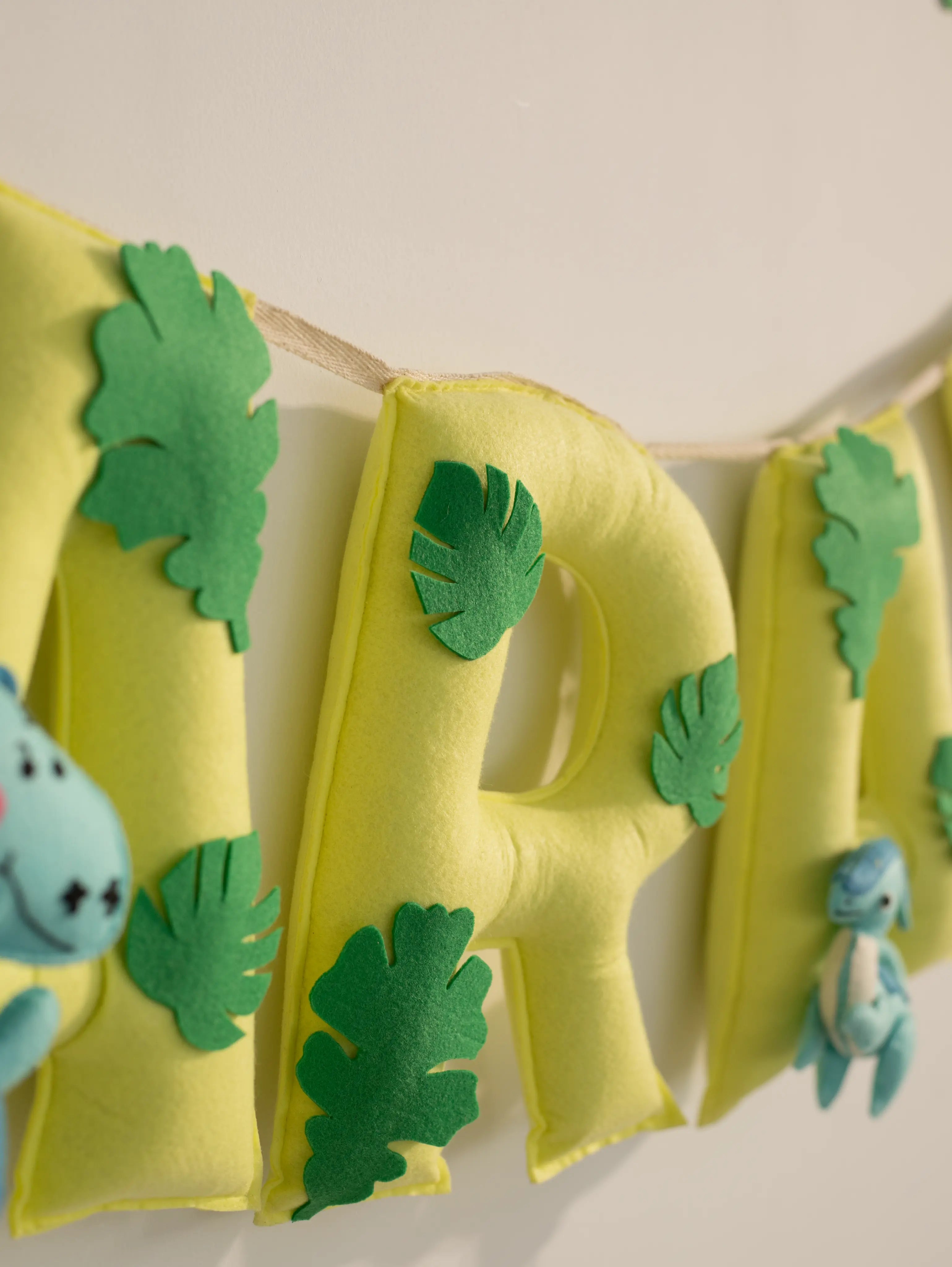 Close-up of the edge section of the personalized Arav felt name banner with handcrafted green leaf embellishments and yellow pennants