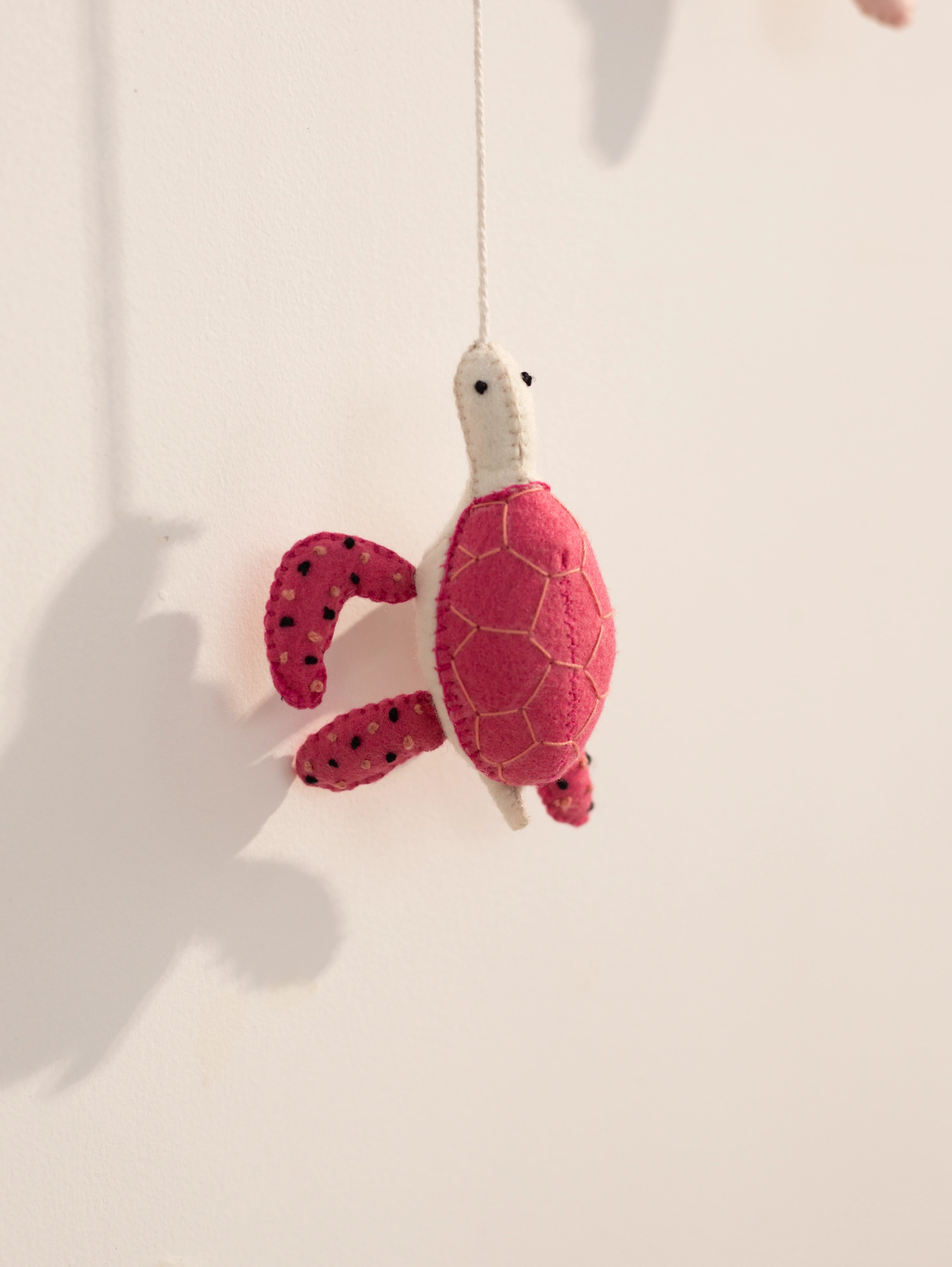 Close-up of a handcrafted red felt sea turtle hanging ornament from a personalized ocean-themed baby nursery name banner