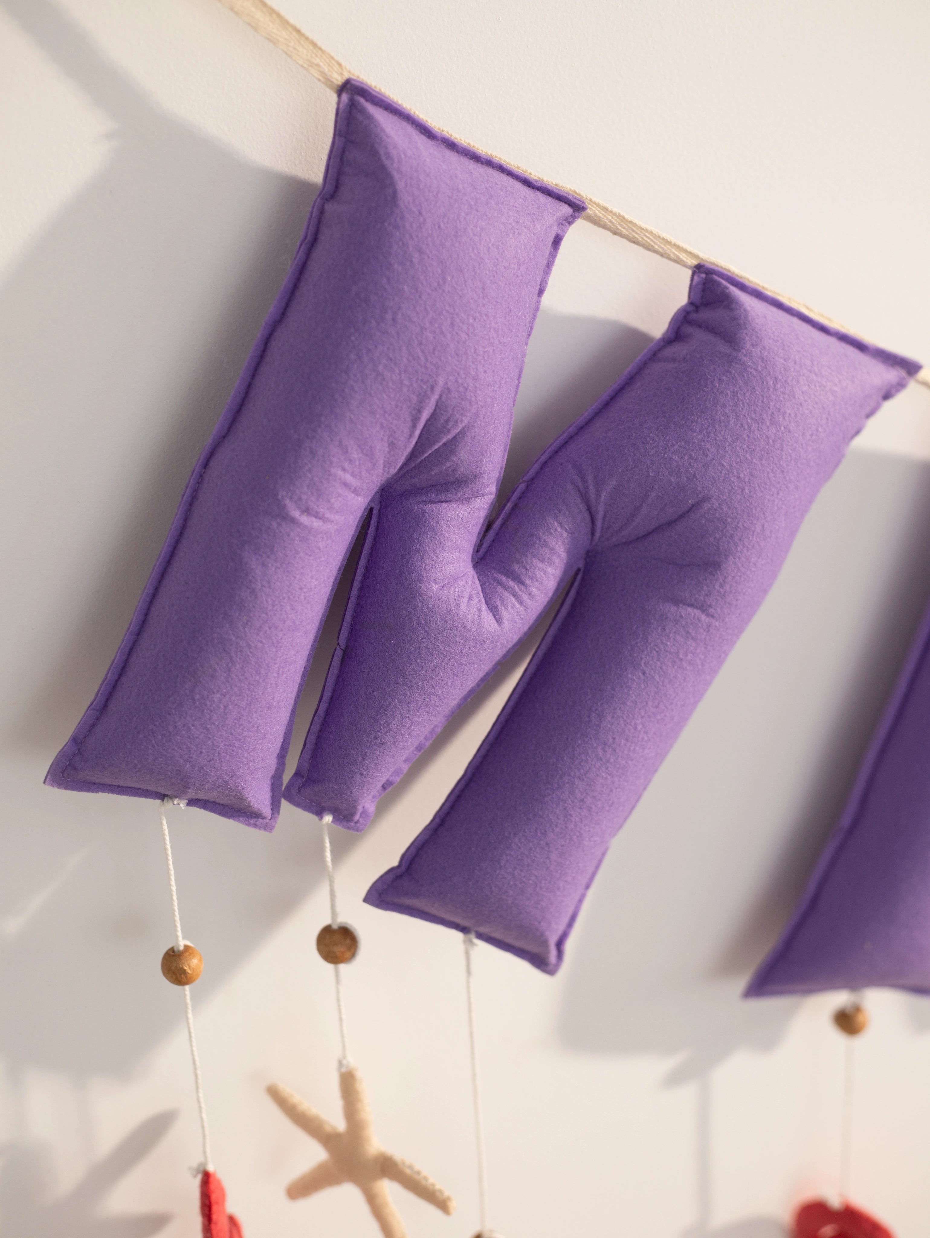 Detailed close-up of the ‘M’ letters on the personalized Miraya felt name banner, handcrafted in purple felt for an ocean-themed nursery