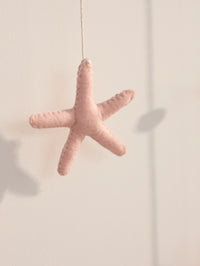 Close-up of a handcrafted pink starfish ornament hanging from the personalized Miraya ocean-themed felt name banner for baby nursery décor.