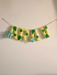 Full view of the personalized Arav felt name banner featuring green and yellow handcrafted letters with playful nursery decorations