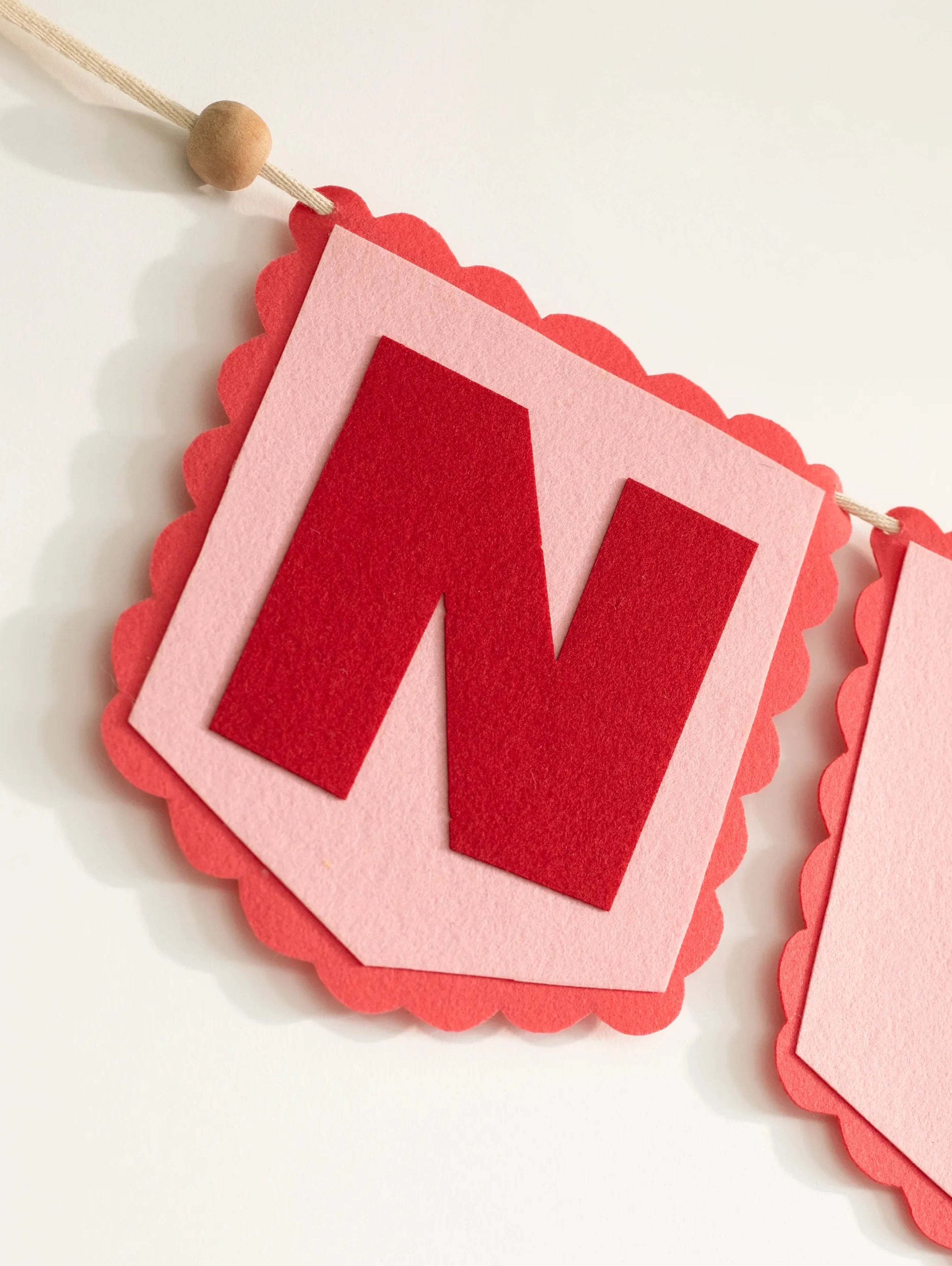 Macro close-up of the handcrafted red felt letter ‘N’ from the personalized Nirvair nursery name banner.