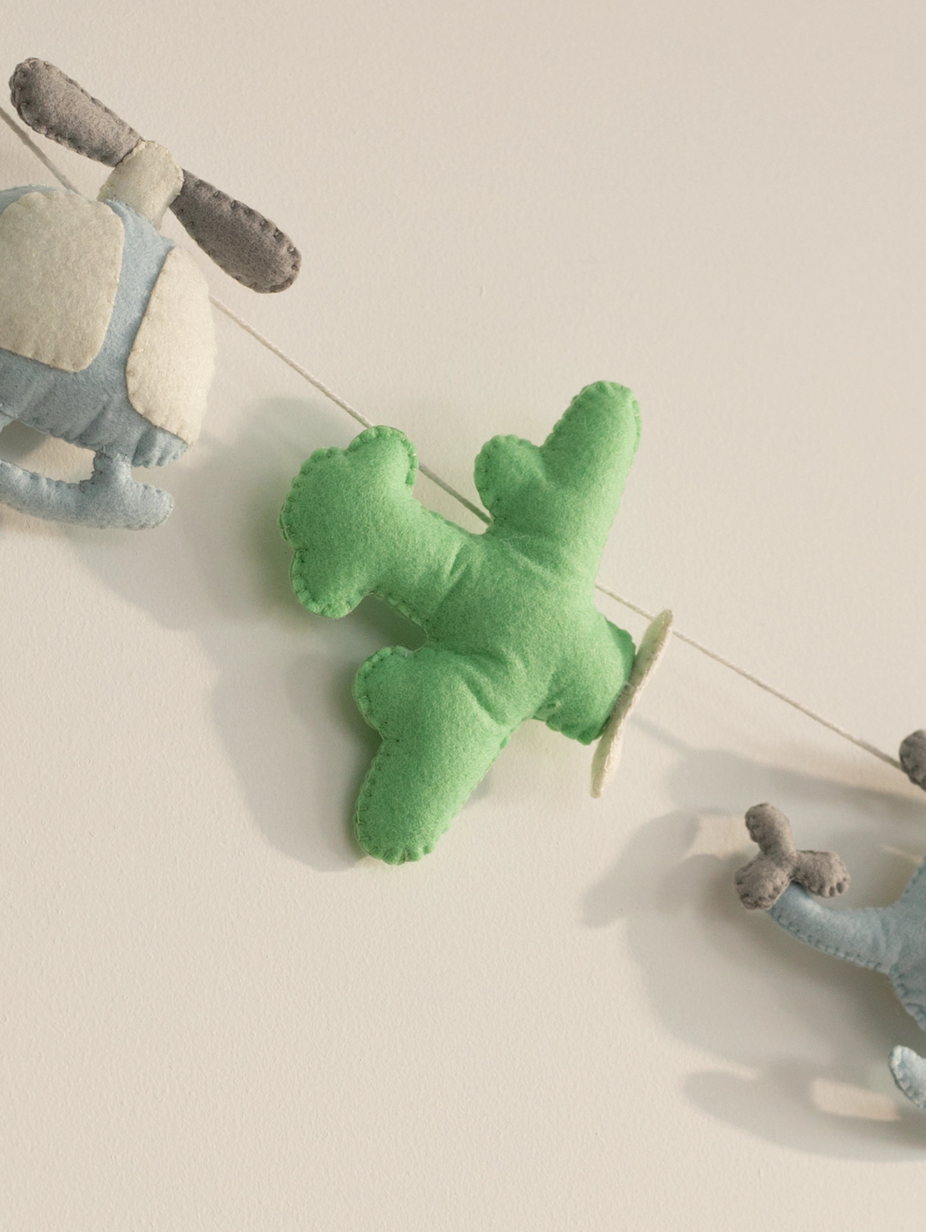 Close-up of a handcrafted pastel green felt airplane from the To The Moon nursery banner with soft stitched detailing.