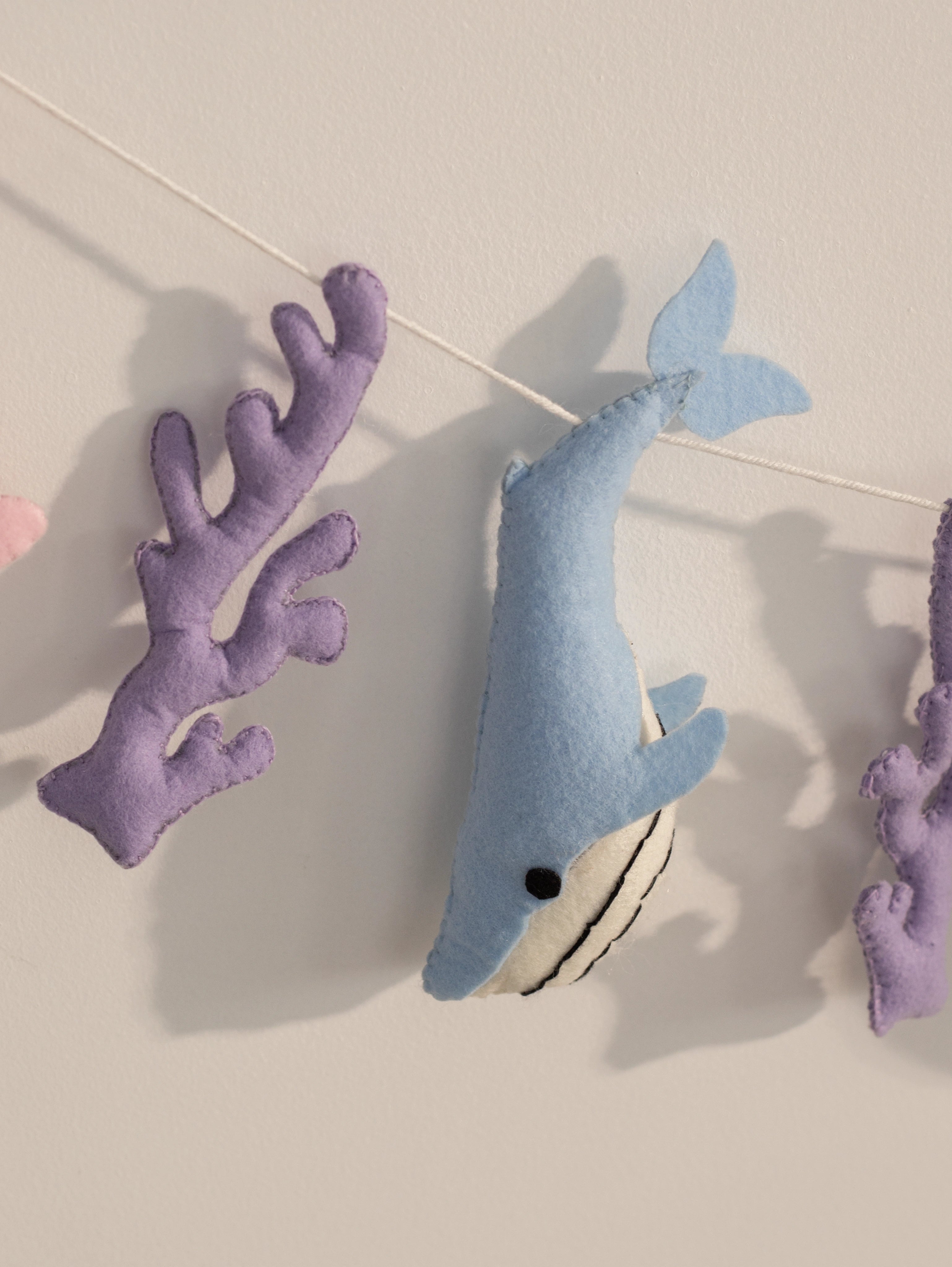 Handcrafted blue felt whale paired with purple coral accents on the Under the Sea nursery banner for playful ocean-inspired wall decor.
