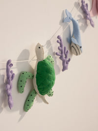 Close-up of the Under the Sea felt banner featuring a plush sea turtle, blue whale and coral accents for coastal nursery decoration.