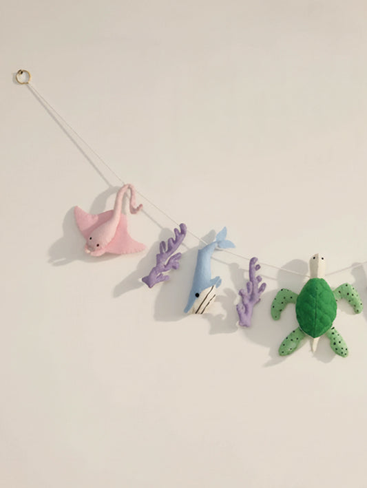 Left-side detail of the Under the Sea felt nursery garland showcasing a pink stingray, blue whale and handcrafted coral elements.