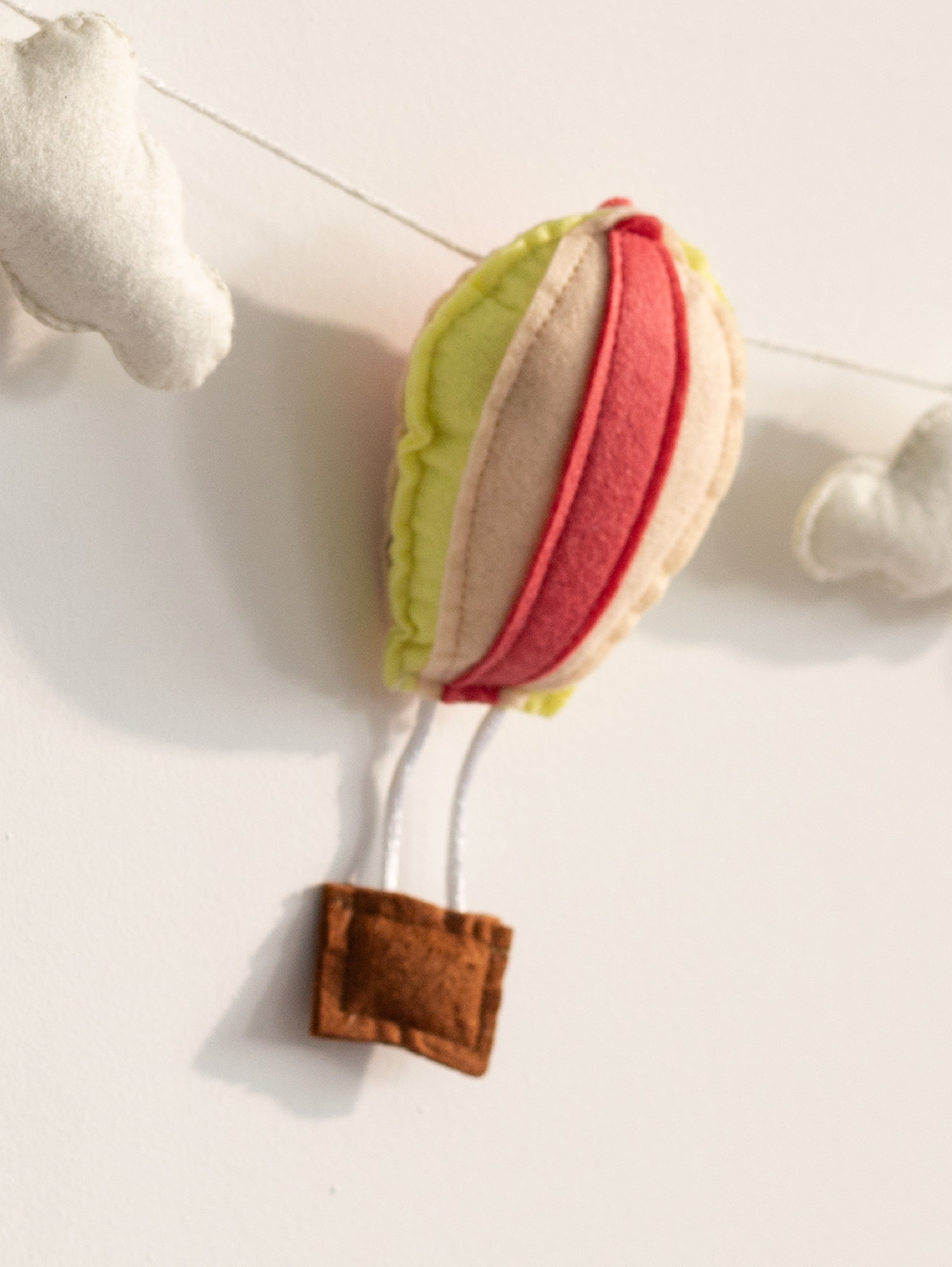 Close-up of a handcrafted felt hot air balloon from the Up and Away nursery banner featuring pastel tones and stitched detailing.