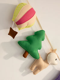 Detailed close-up of the woodland-themed end of a handmade felt name banner featuring a soft deer, pine tree, and pastel hot air balloon for nursery wall decor.